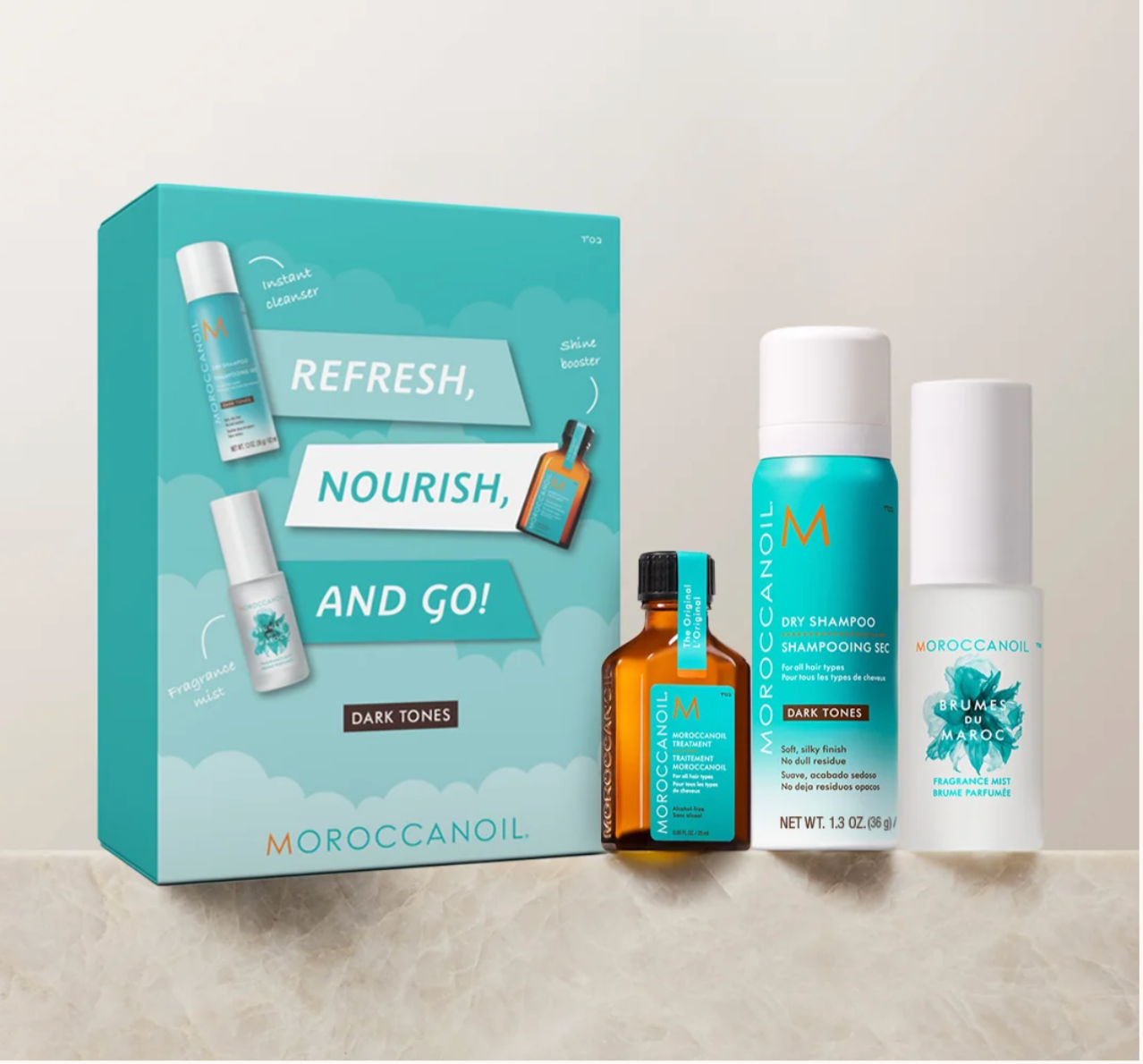 Moroccanoil hair care gift set featuring a teal and white box labeled 'Refresh, Nourish, and Go!' alongside a dark tones shampoo bottle, a dark tones shampooing oil bottle, and a dark tones leave-in bottle, arranged on a light marble surface against a neutral beige background.