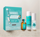 Moroccanoil hair care gift set featuring a teal and white box labeled 'Refresh, Nourish, and Go!' alongside a dark tones shampoo bottle, a dark tones shampooing oil bottle, and a dark tones leave-in bottle, arranged on a light marble surface against a neutral beige background.
